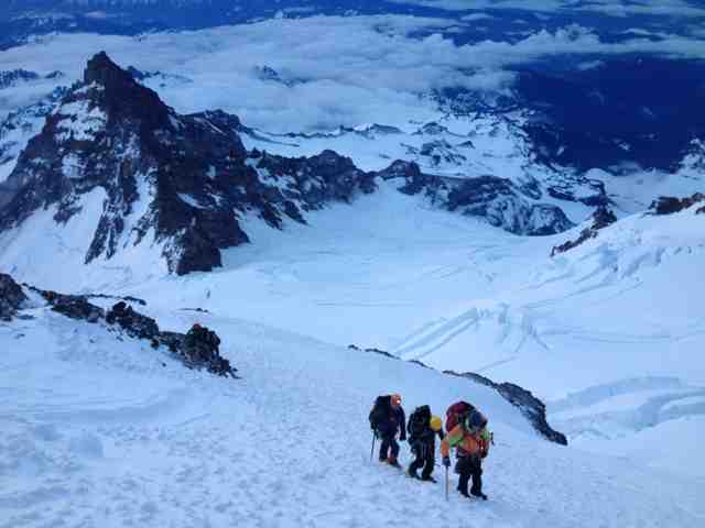 A hiker overlooking a pristine, icy blue glacier lake in the mountains.